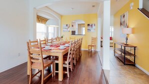 A dining area with a long wooden table set for six, surrounded by wooden chairs.