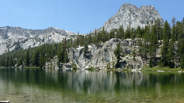 Ein Bergsee mit klarem Wasser, umgeben von felsigen Klippen und dichten Wäldern.