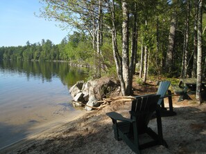 A lakeside setting with a bench and picnic table, surrounded by trees and a calm body of water. - Meddybemps Lake House with. Sandy Beach Cool Summer Temps, highs in the 70s.  (Alexander)