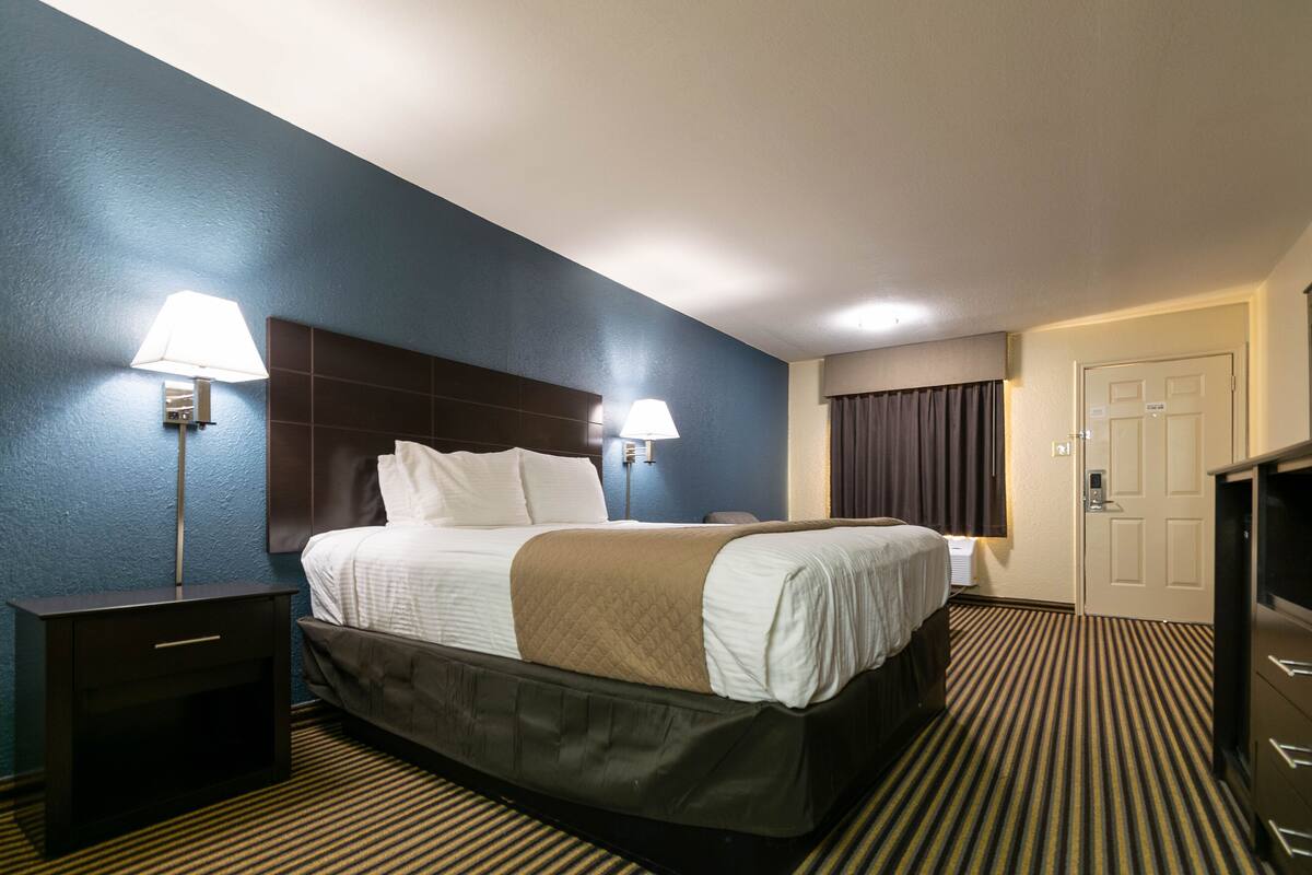 A hotel room with a bed, bedside lamps, a nightstand, a dresser, and a door.