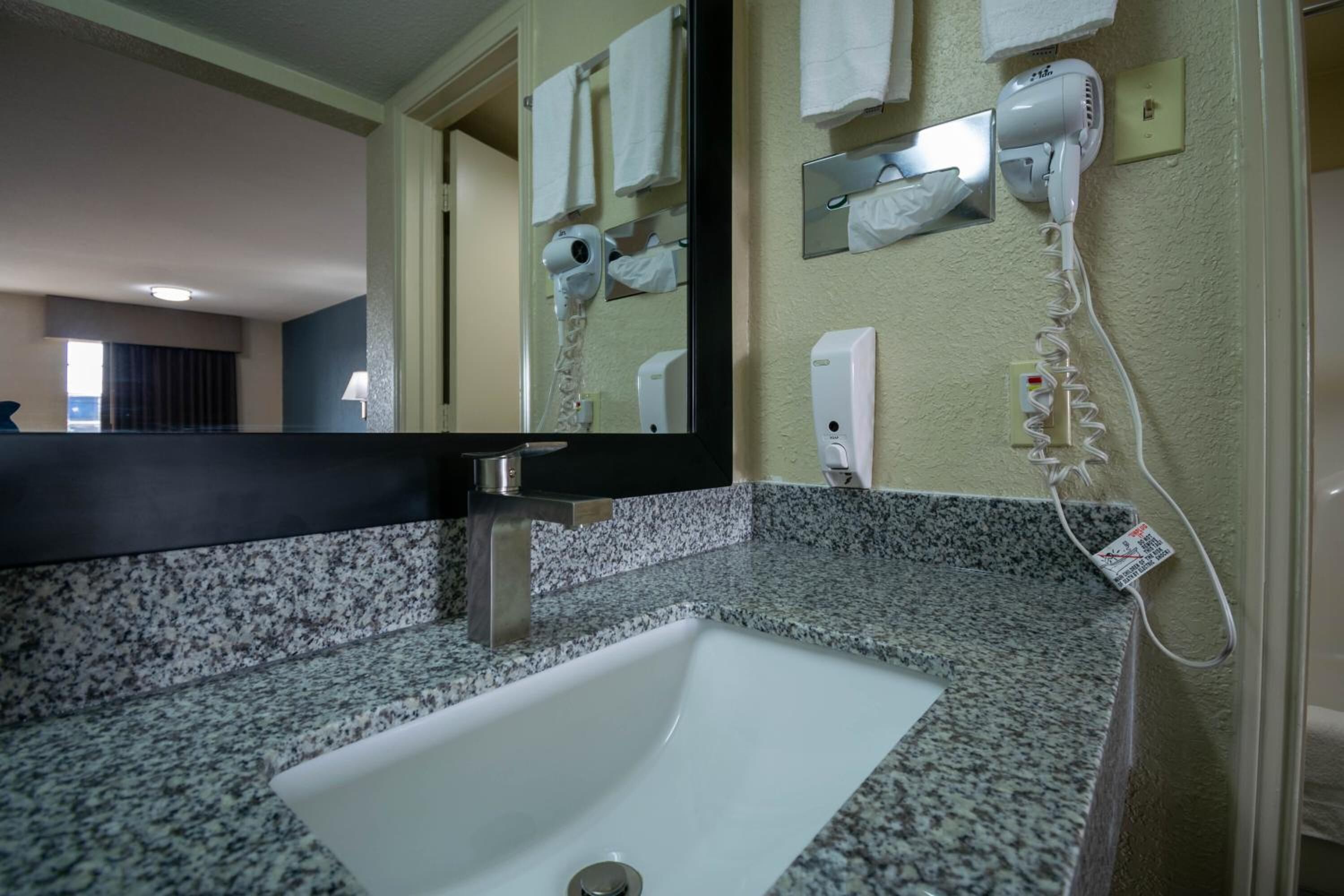 A bathroom with a granite countertop, a white sink, a mirror, a towel rack, and a hairdryer.