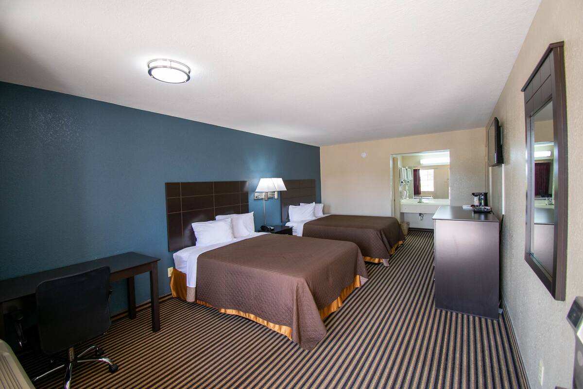 A hotel room with two beds, a desk, a chair, a dresser, and a mirror.