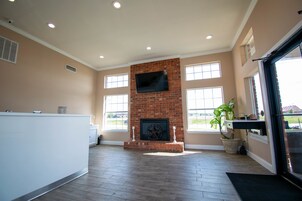 A spacious living room with a brick fireplace, large windows, and a flat-screen TV mounted above it.