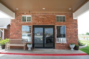 A brick building with a glass door entrance, a bench, and potted plants.