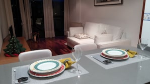 Un coin repas avec une table mise pour deux, comprenant des assiettes, des couverts et un verre. On aperçoit un sapin de Noël à l’arrière-plan.