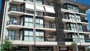 Un immeuble à plusieurs étages doté de balcons, un café appelé « Perla 5 » situé au rez-de-chaussée, et une échelle de secours bien visible.