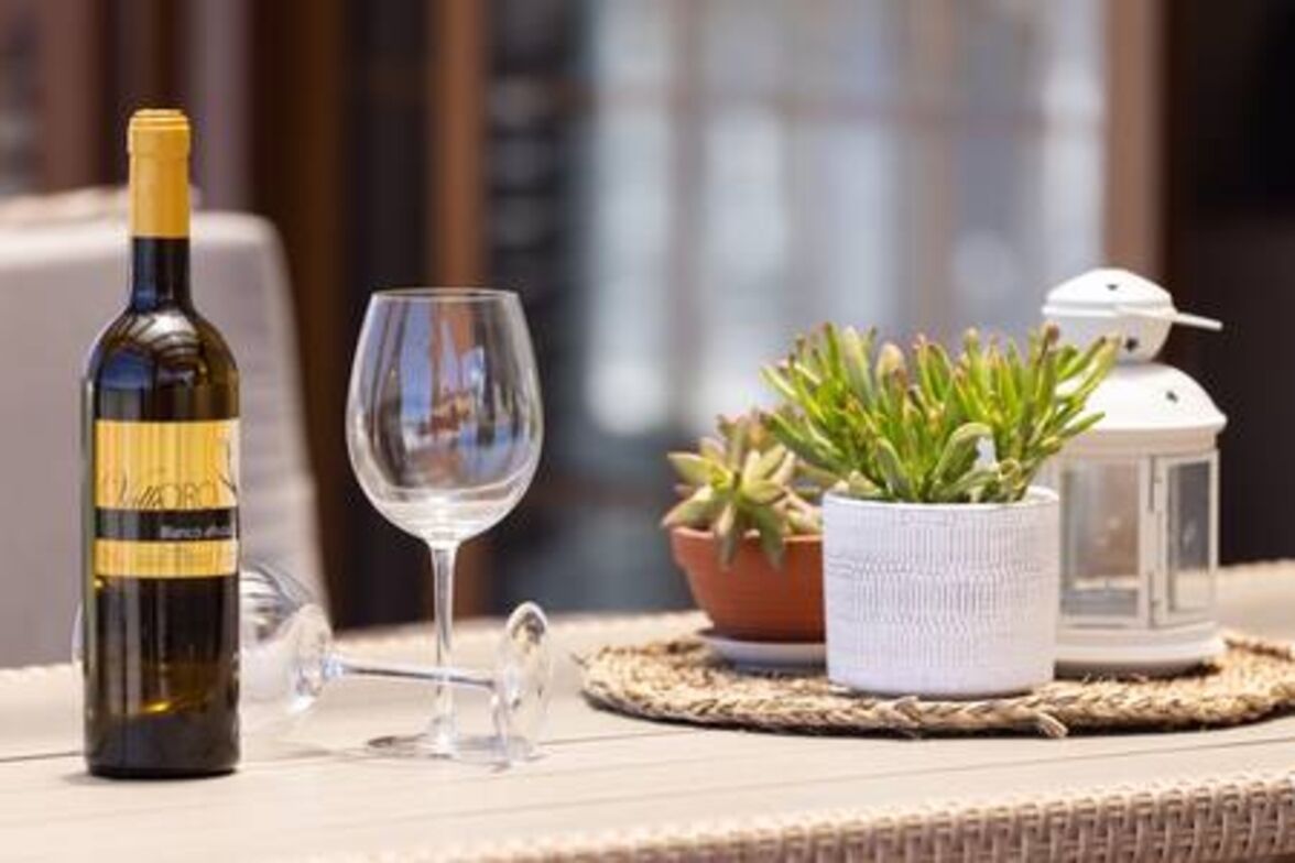 Een fles wijn, een wijnglas, een bloempot en een lantaarn op een tafel.