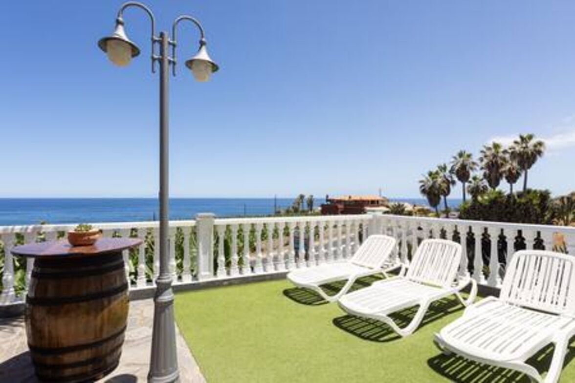 Een balkon met witte stoelen, een houten vat en een lantaarn.