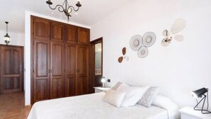 A bedroom with a large bed, a wooden wardrobe, a bedside table, and wall decor. - Home2Book Garachico Ocean View & Wifi (Las Cruces)