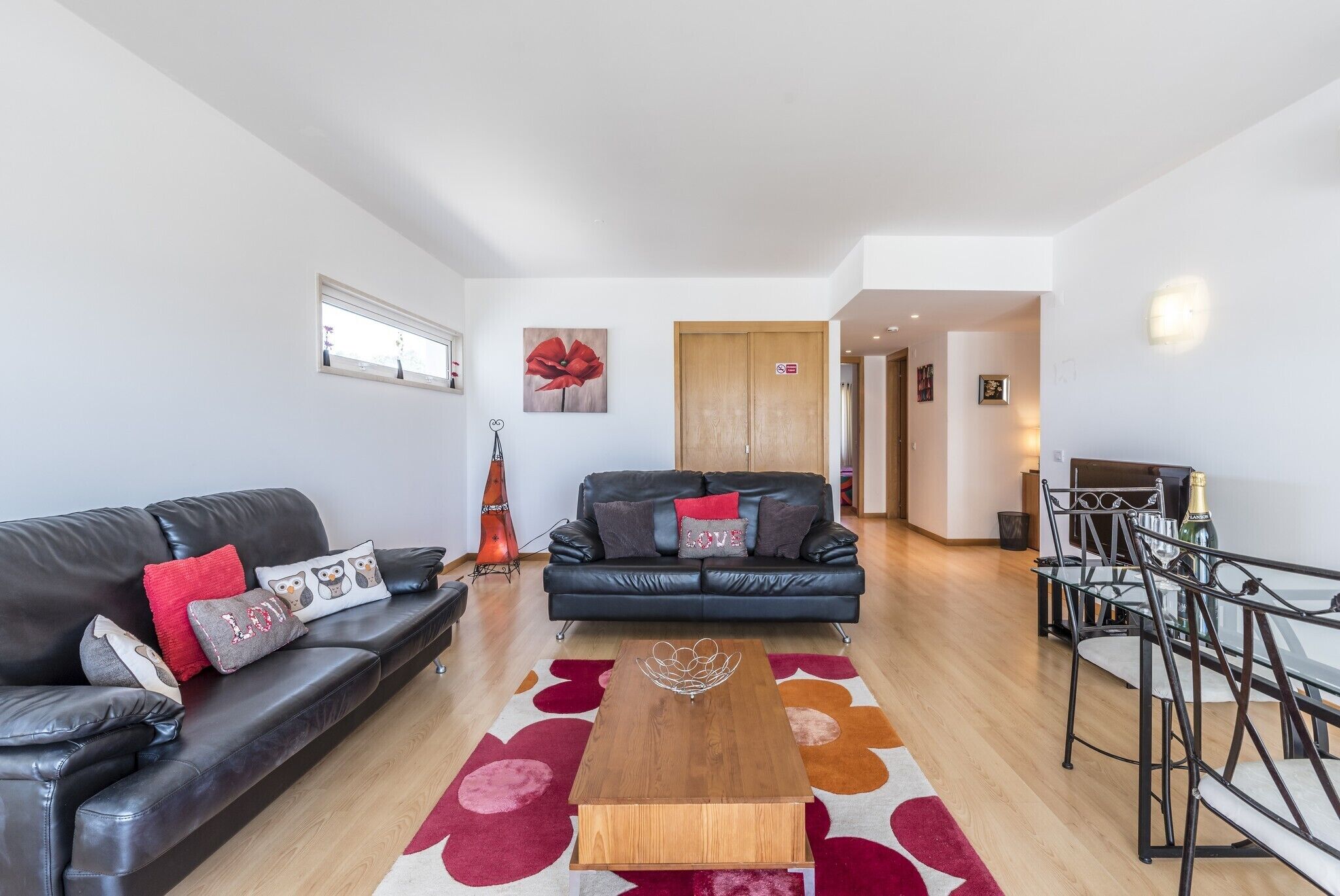 A modern living room with a black leather sofa, a wooden coffee table, and a glass dining table with metal chairs.