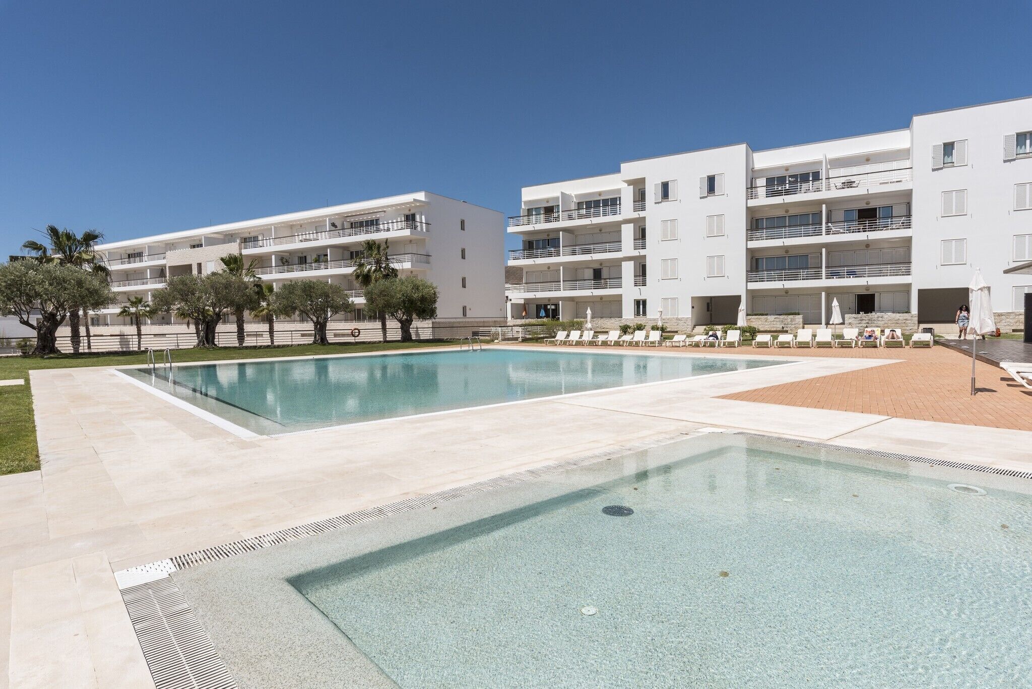A modern hotel with a swimming pool, multiple balconies, and lounge areas.