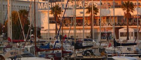 A marina with multiple boats docked, a building with 'MARINA DE LAGOS' signage, and palm trees in the background.