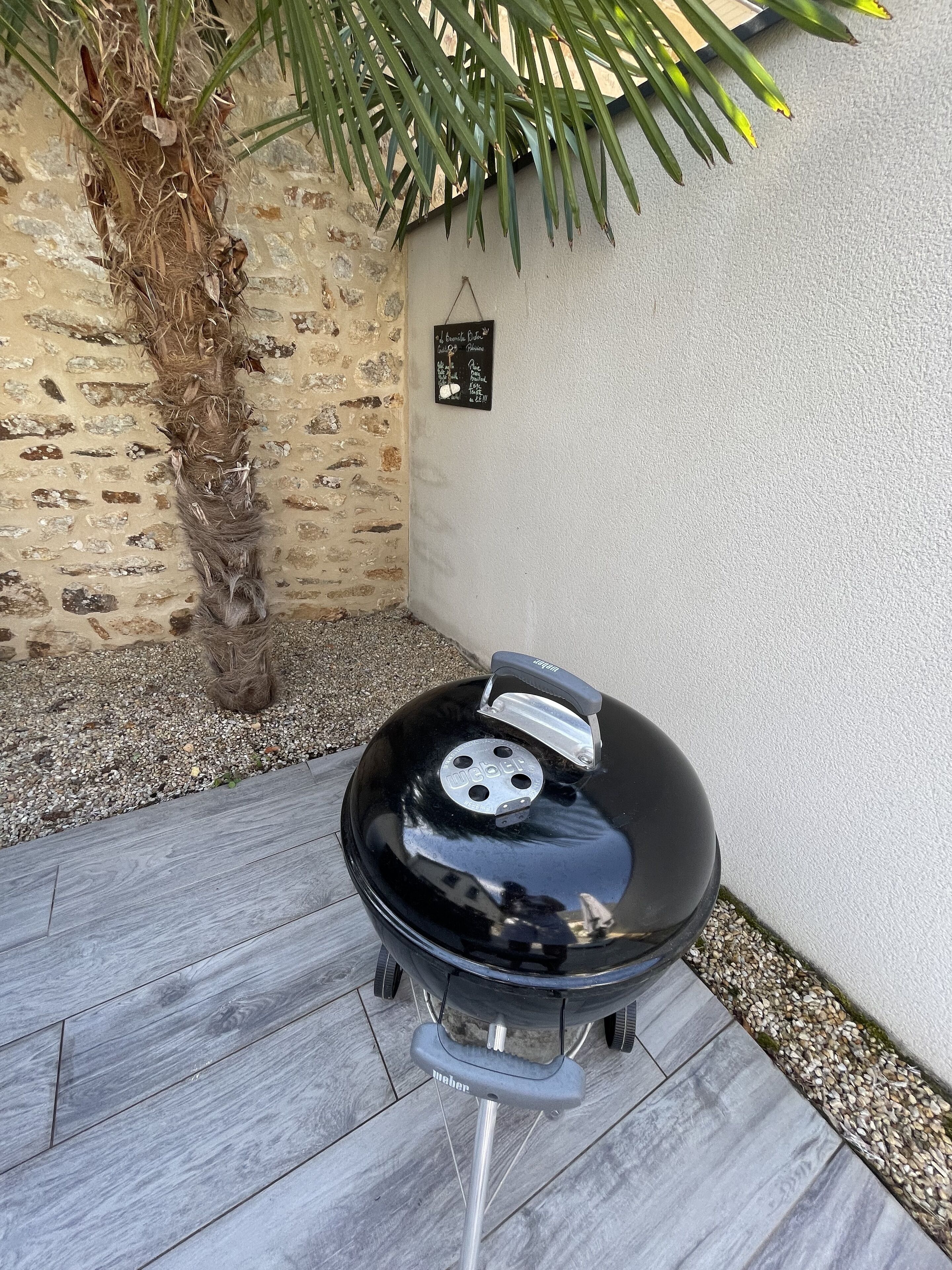 A Weber grill with a black lid, positioned on a patio with grey tiles and a stone wall.