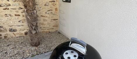 A Weber grill with a black lid, positioned on a patio with grey tiles and a stone wall.