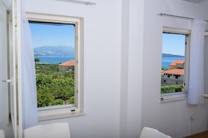 Una habitación con dos ventanas, una de las cuales ofrece vistas a una zona costera con edificios y vegetación.