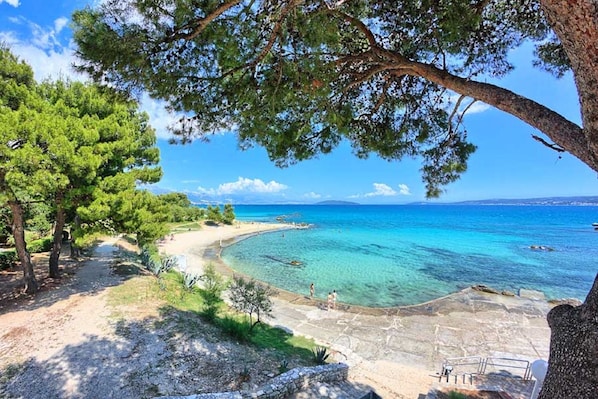 Un sendero costero que lleva a una playa con aguas turquesas cristalinas y una vista distante del mar.