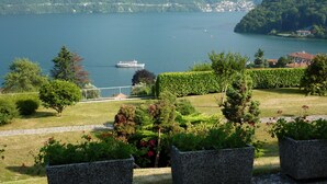 A lake with a boat, surrounded by mountains and a well-maintained garden with hedges and potted plants.
