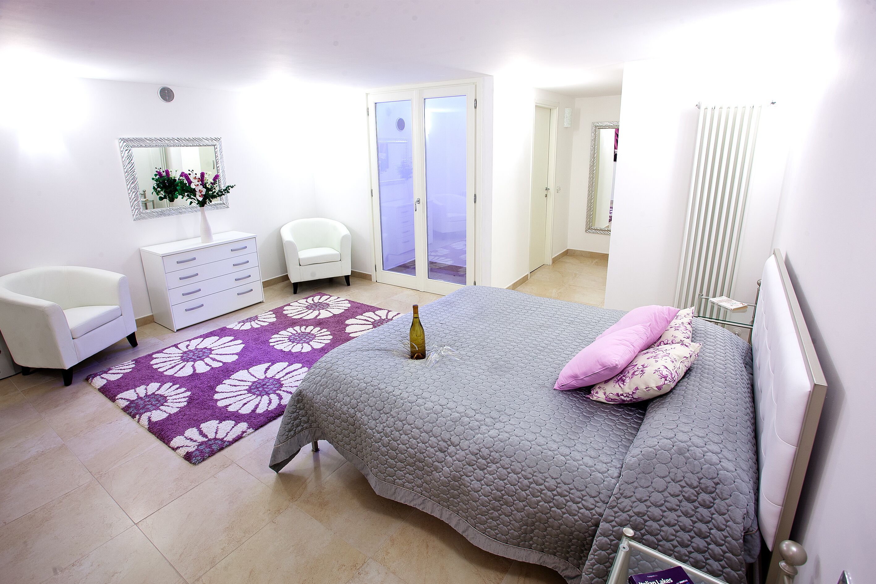 Ein Schlafzimmer mit Bett, Kommode, Stuhl, Spiegel und einer Tür zu einem weiteren Raum.