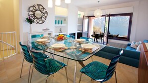 A modern dining area with a glass table, teal chairs, and a view of the outdoors through large windows.