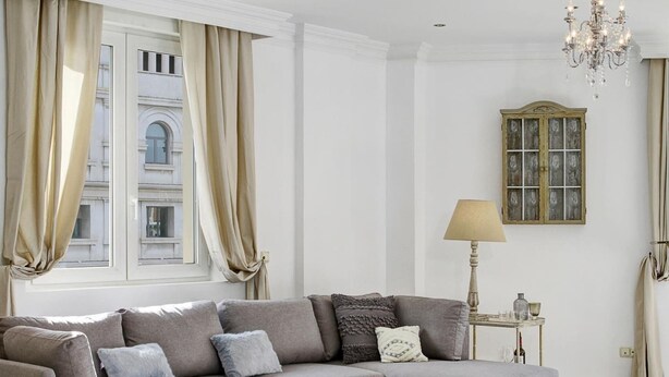 A living room with a sectional sofa, a small table, a lamp, and a window with curtains. - ChezmoiHomes La Belle Epoque (Granada)
