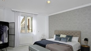 A bedroom with a bed, bench, wardrobe, and a view of a building through a window. - ChezmoiHomes La Belle Epoque (Granada)