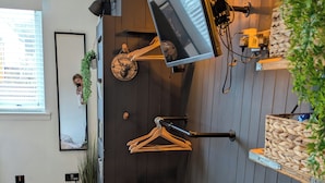 Een kamer met een houten bank, een hangende televisie en een wandrek met kleding.