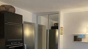 Ett modernt kök med ett svart kylskåp, en ugn och en vit bänkskiva. I vardagsrummet finns en svart soffa och ett vitt soffbord.