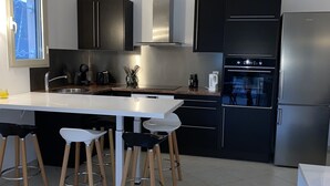 Ett modernt kök med en central köksö, svarta skåp, vitvaror i rostfritt stål och ett fönster med fin utsikt.