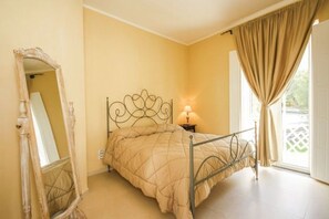 Ein Schlafzimmer mit einem Bett, einem Nachttisch, einer Lampe, einem Spiegel und einem Fenster mit Vorhängen.