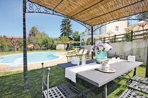 Un espace extérieur abrité, aménagé pour les repas, avec une piscine, des tables, des chaises et un vase décoratif.
