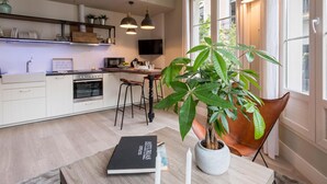 A modern kitchen with white cabinets, a dining area with a table and chairs, and a large potted plant. - ChezmoiHomes Trinidad Deluxe 1 (Granada)