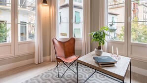 A room with a leather chair, a table with books and a potted plant, and large windows with curtains. - ChezmoiHomes Trinidad Deluxe 1 (Granada)