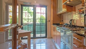 A modern kitchen with a gas stove, wooden cabinets, and a glass door leading to a balcony. - CARCAVELOS BEACH 2. A wonderful 2 bedroom (Carcavelos)