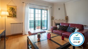 A living room with a red sofa, a coffee table with decorative items, a radiator, and a large window with curtains. - CARCAVELOS BEACH 2. A wonderful 2 bedroom (Carcavelos)