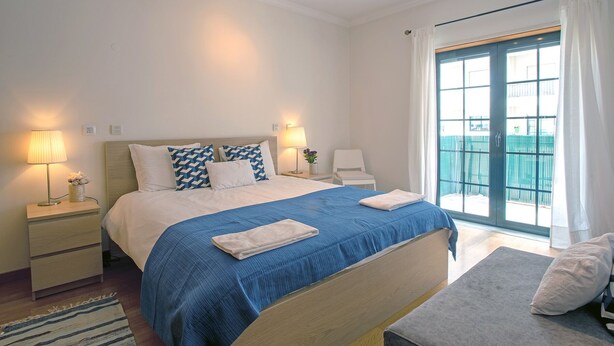 A hotel room with a large bed, two bedside tables, a nightstand, a window with curtains, and a view of the outside. - CARCAVELOS BEACH 2. A wonderful 2 bedroom (Carcavelos)