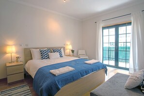 A hotel room with a large bed, two bedside tables, a nightstand, a window with curtains, and a view of the outside. - CARCAVELOS BEACH 2. A wonderful 2 bedroom (Carcavelos)