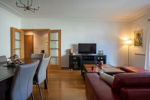 Un salon moderne avec un téléviseur, un canapé rouge, une table à manger avec des chaises et une porte en bois.