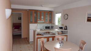 A compact kitchen with a refrigerator, microwave, and coffee maker. There is a dining table with chairs and a clock on the wall. - App. Les Roches d'Argent-Sea View, Beaches, Heated Indoor Pool. (Plestin-Les-Grèves)