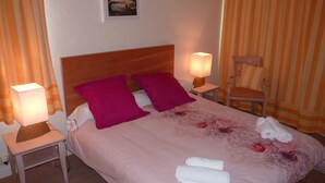 A neatly made bed with pink bedding, two pillows, and two rolled towels. There are two bedside lamps, a chair, and a small table with a lamp. - App. Les Roches d'Argent-Sea View, Beaches, Heated Indoor Pool. (Plestin-Les-Grèves)