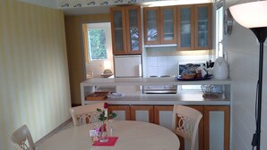 A kitchen with wooden cabinets, a white countertop, and a dining table with chairs. - App. Les Roches d'Argent-Sea View, Beaches, Heated Indoor Pool. (Plestin-Les-Grèves)
