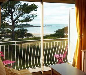 A balcony with a view of the sea, a table, and two chairs.