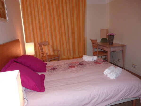 A hotel room with a bed, two chairs, a desk, and a lamp.