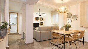 Una sala de estar moderna con un sofá, una mesa de comedor y sillas. Hay un televisor y una planta en la esquina.