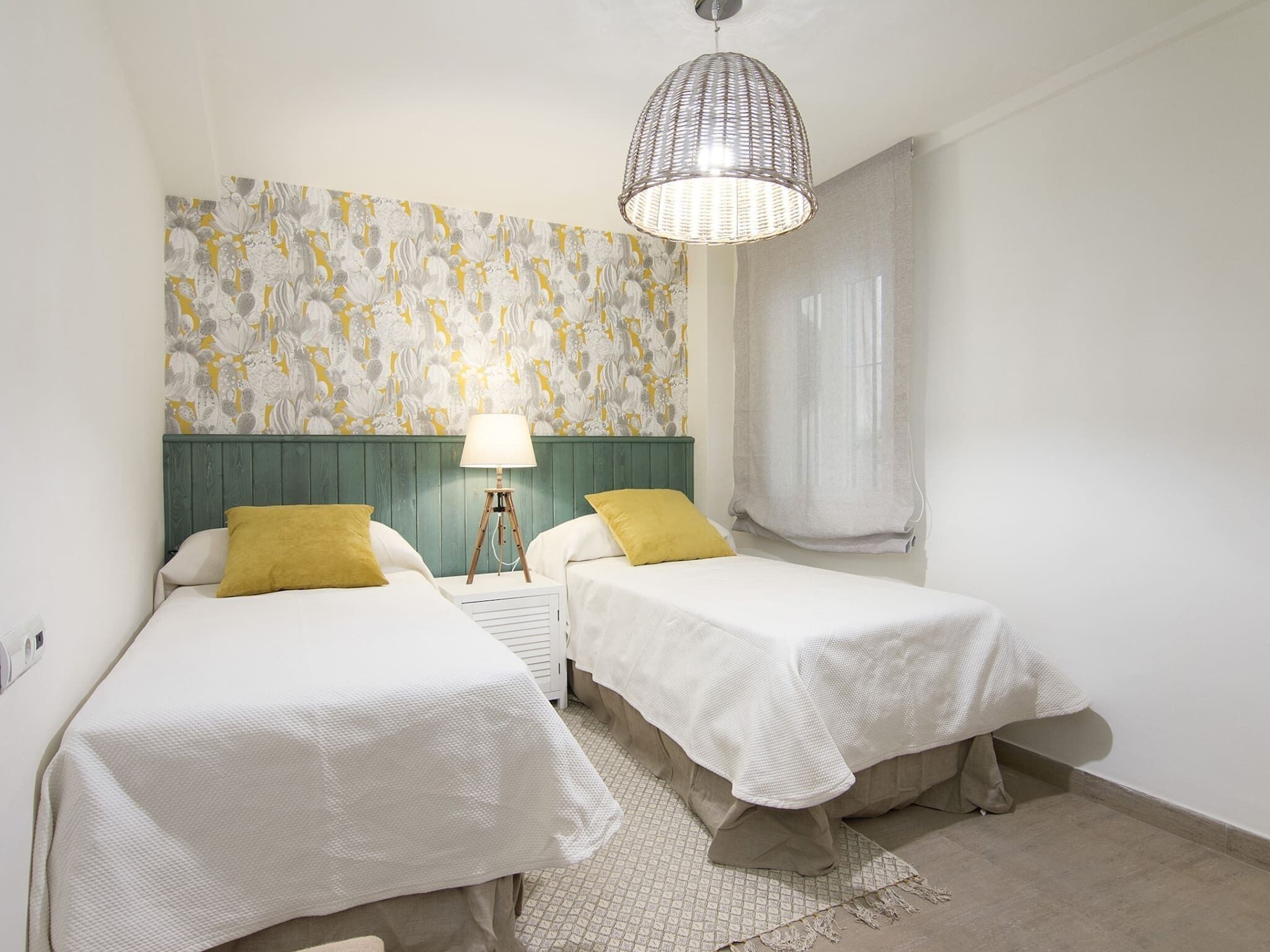 Un dormitorio con dos camas, un papel tapiz estampado, una lámpara colgante y una ventana con cortinas.