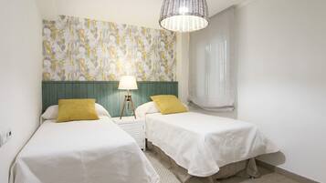 Un dormitorio con dos camas, un papel tapiz estampado, una lámpara colgante y una ventana con cortinas.