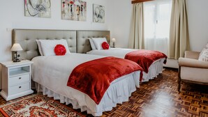 A hotel room with two beds, a nightstand, a chair, a window with curtains, and artwork on the wall. - Funchal City View Gardens I  (Funchal)