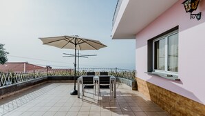 An outdoor patio with a table and chairs, a large umbrella, and a view of the sea. - Funchal City View Gardens I  (Funchal)