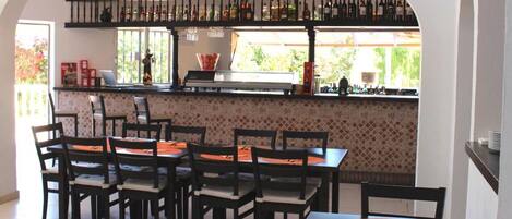 Ein Restaurant mit Fliesenboden, Holztischen und -stühlen, einer Bar mit Flaschen und Blick durch große Fenster.