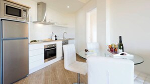 Une cuisine moderne équipée d  ’un four encastré, d’un micro-ondes et d’un lave-vaisselle. On y trouve également un coin repas avec une table en verre et des chaises blanches.