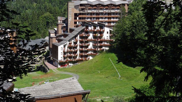 Un hotel de varios pisos con balcones, con vistas a montañas y un bosque denso.